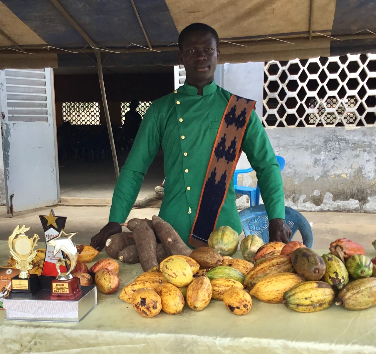Le jeune Mambo Sika présentant des produits agricoles locaux dans un stand.